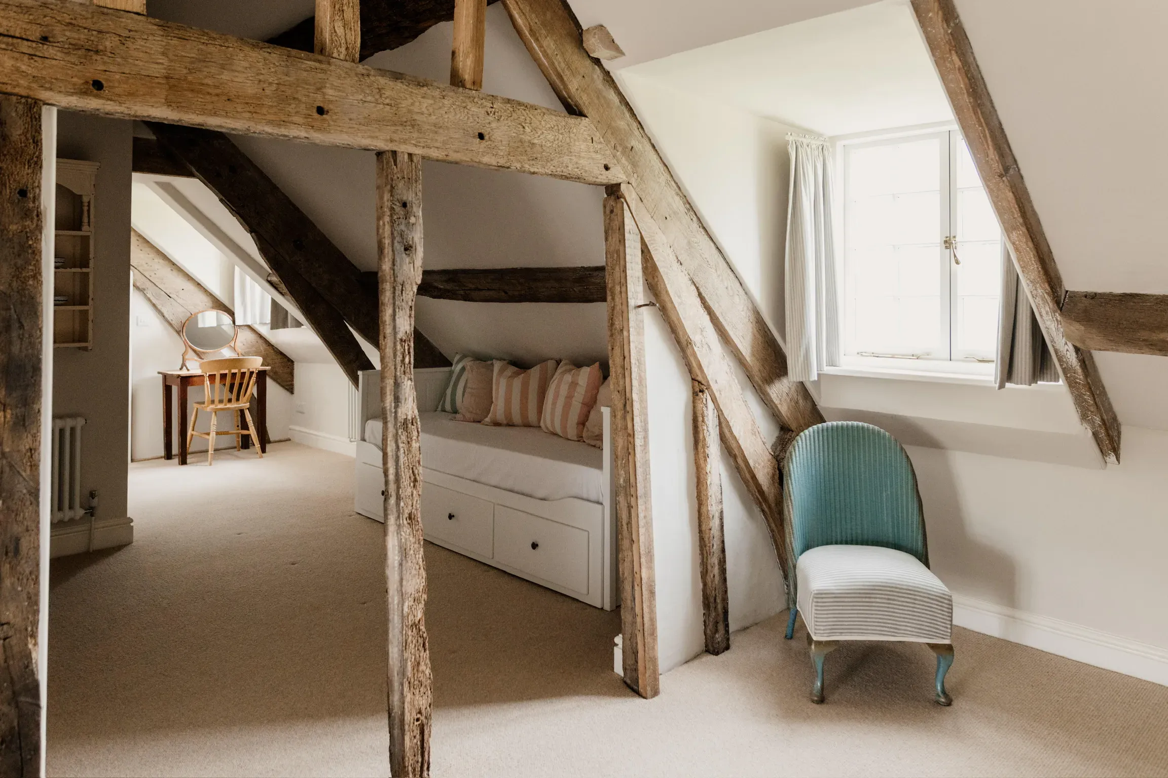 Attic bedroom in a restored listed building, with exposed oak beams and a window seat