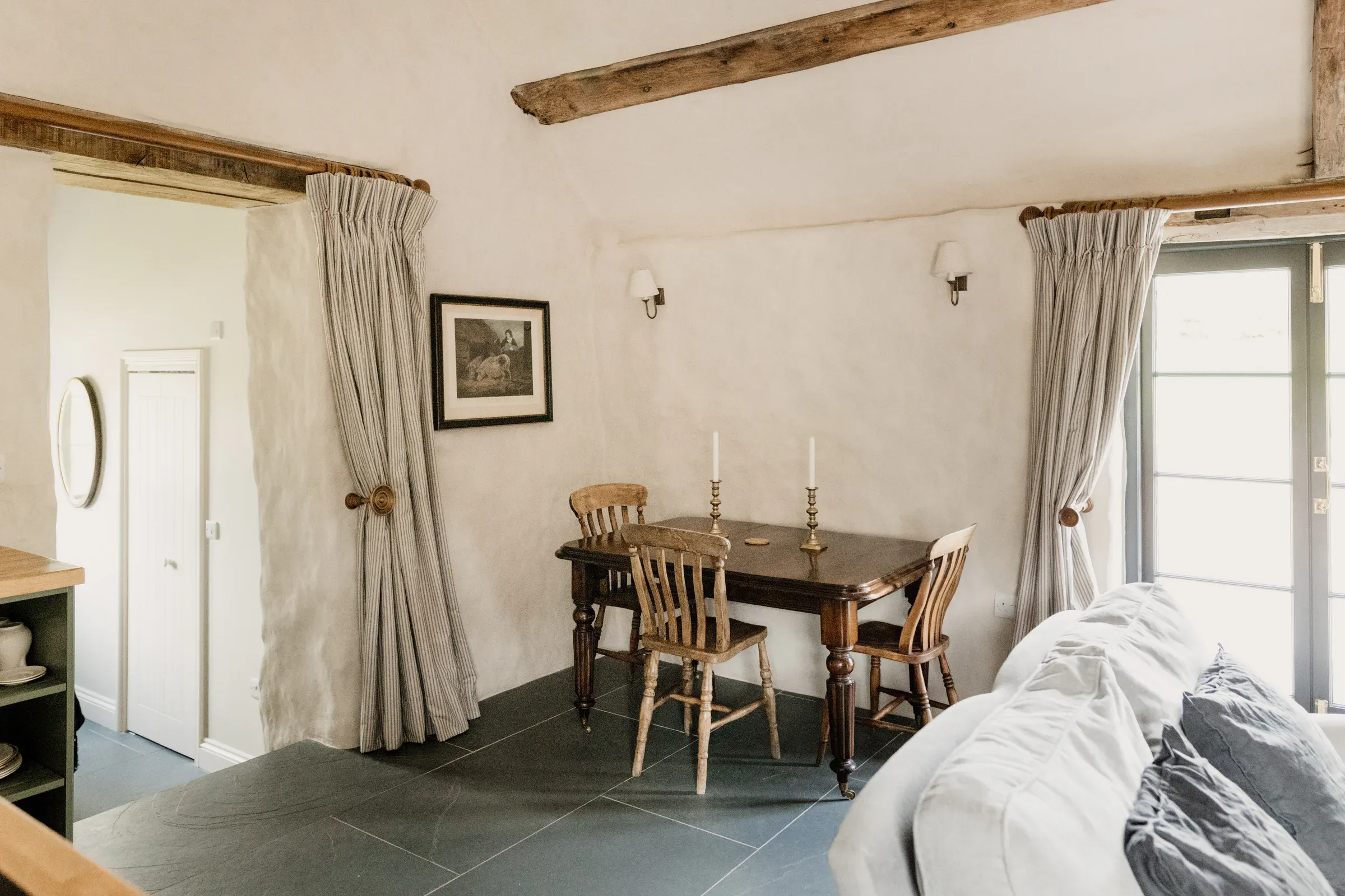 Living and dining room in a converted stone barn near Abergavenny, with limewashed walls, exposed beams and a flagstone floor