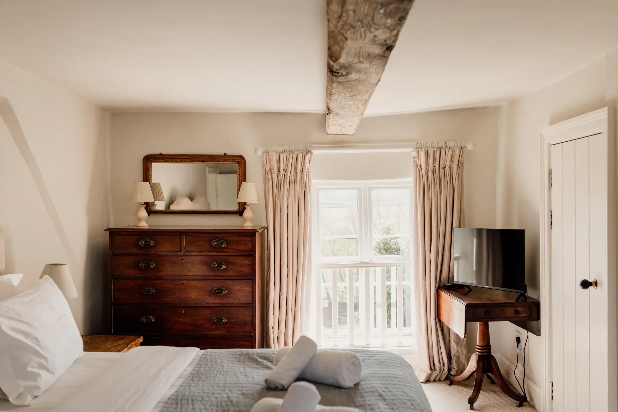 Bedroom with lime-plastered walls, a ceiling beam and a window onto the countryside
