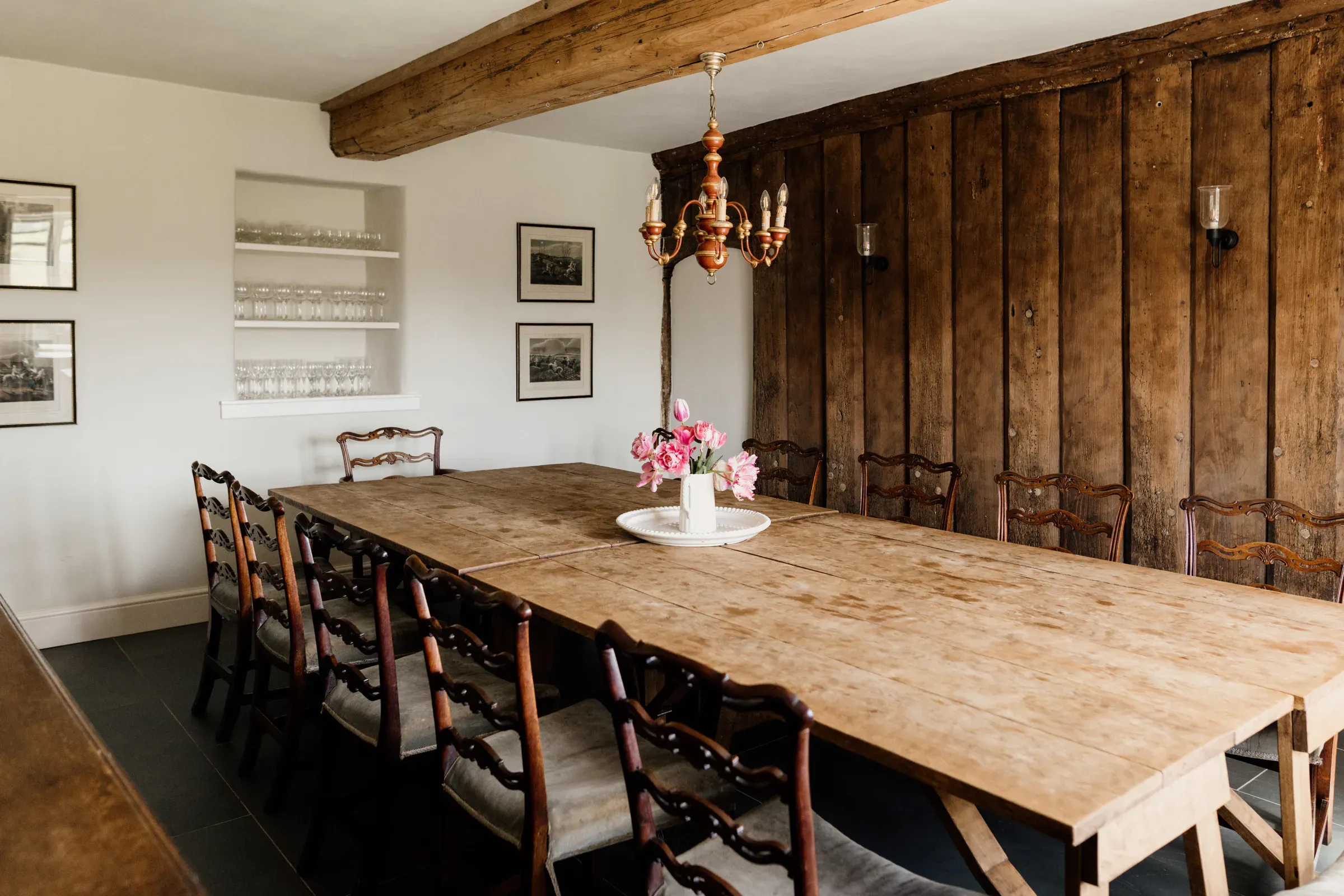 Long dining table with ladderback chairs against a restored timber-framed wall