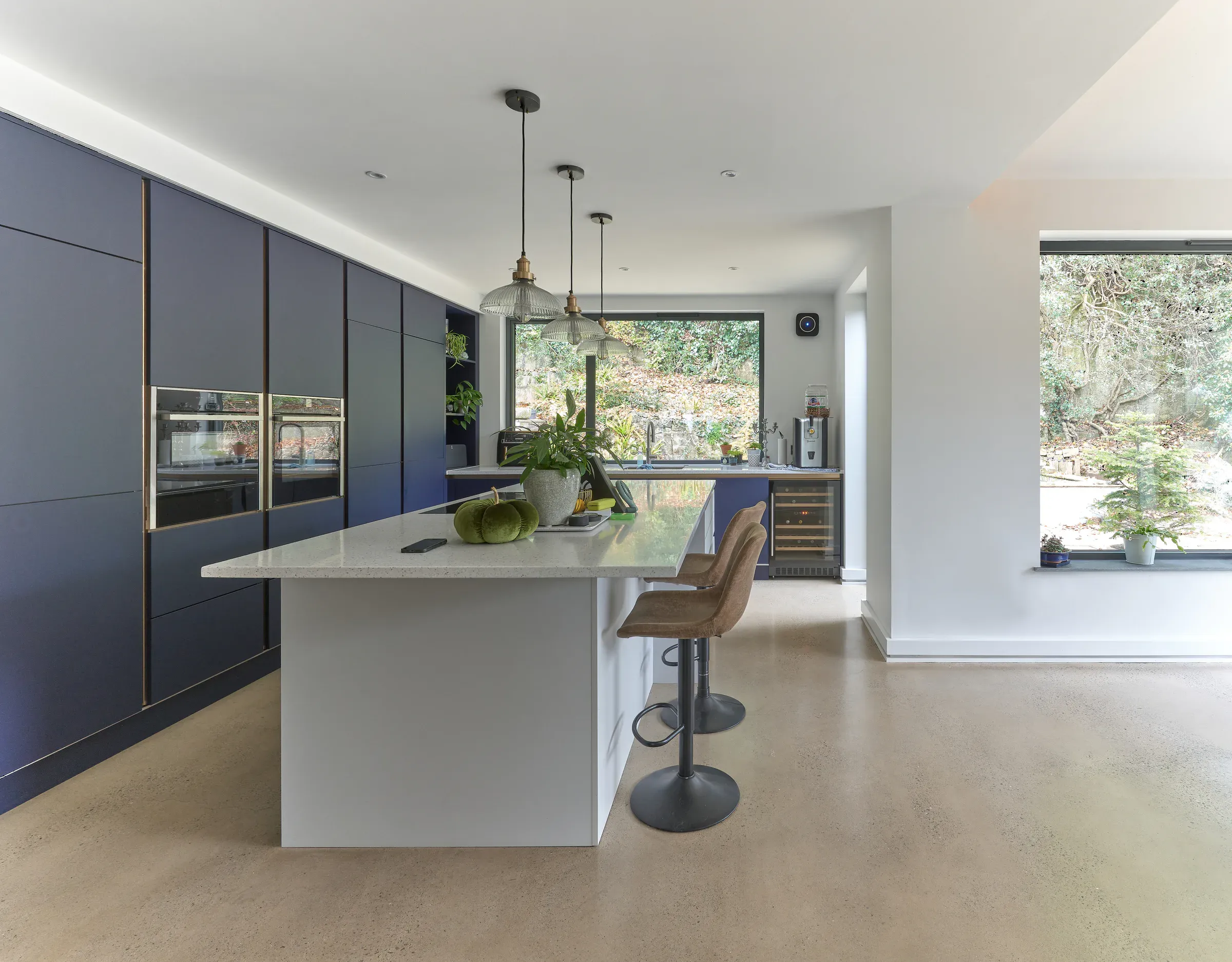 Hand-finished kitchen with navy units, a white island and bar stools, and a vista window onto the garden