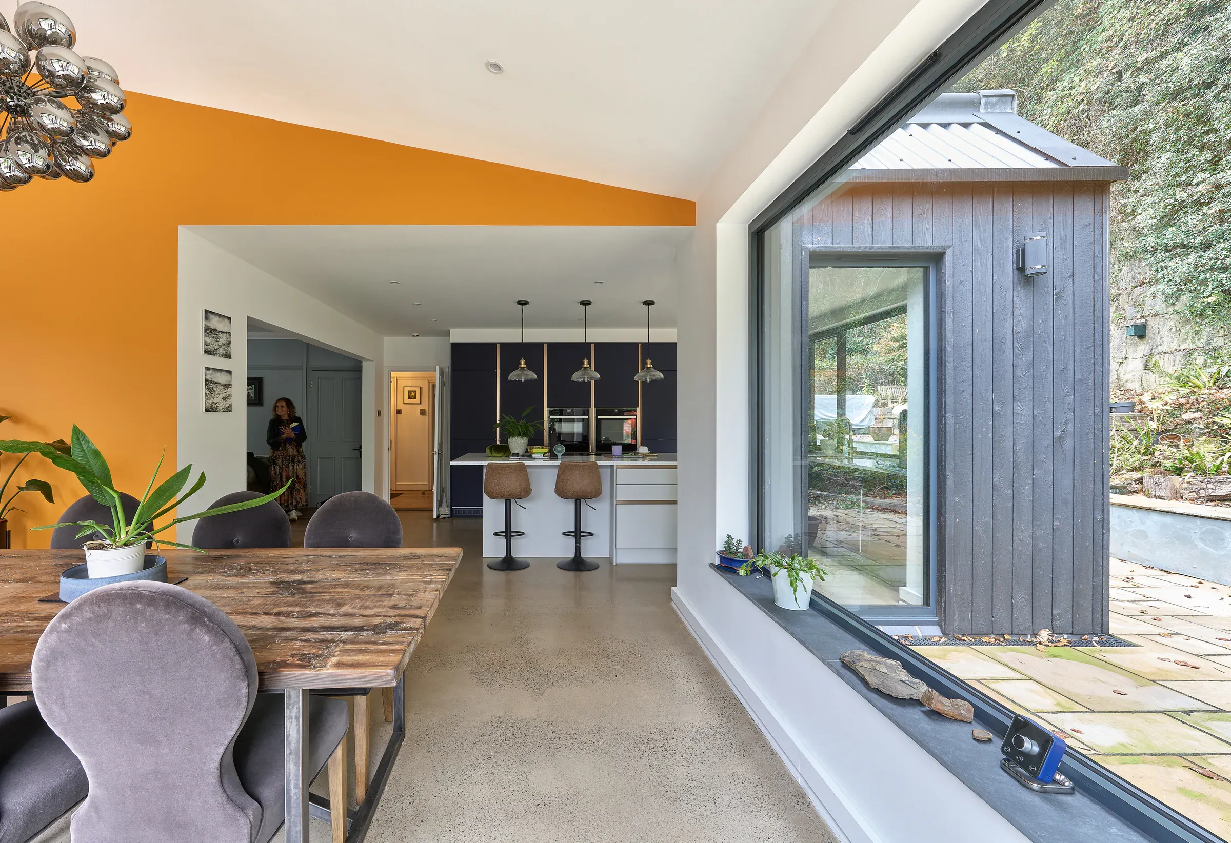 Dining area with a reclaimed timber table, an orange feature wall and doors open to the garden