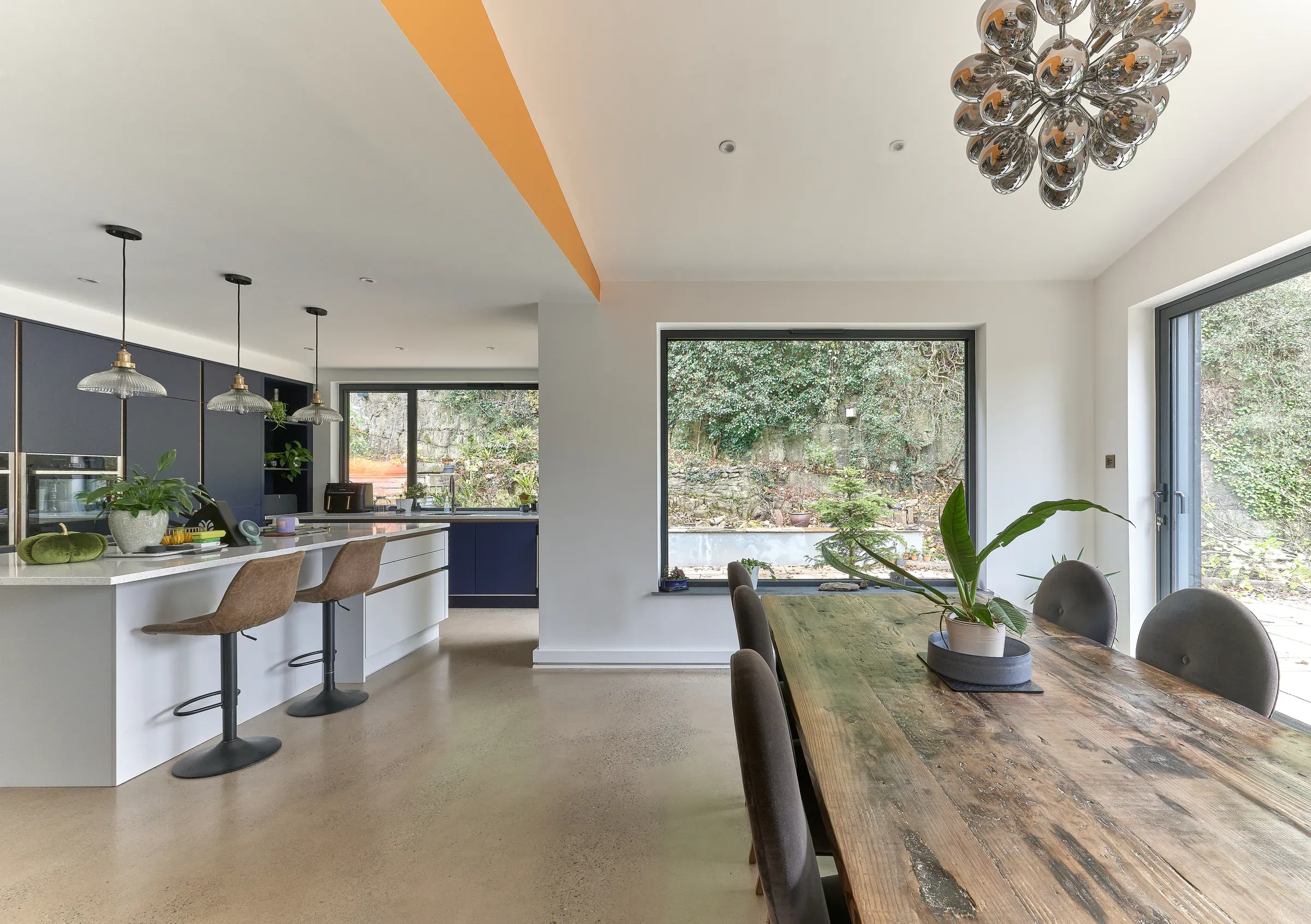 Reclaimed timber dining table beneath an angled ceiling, with the kitchen beyond