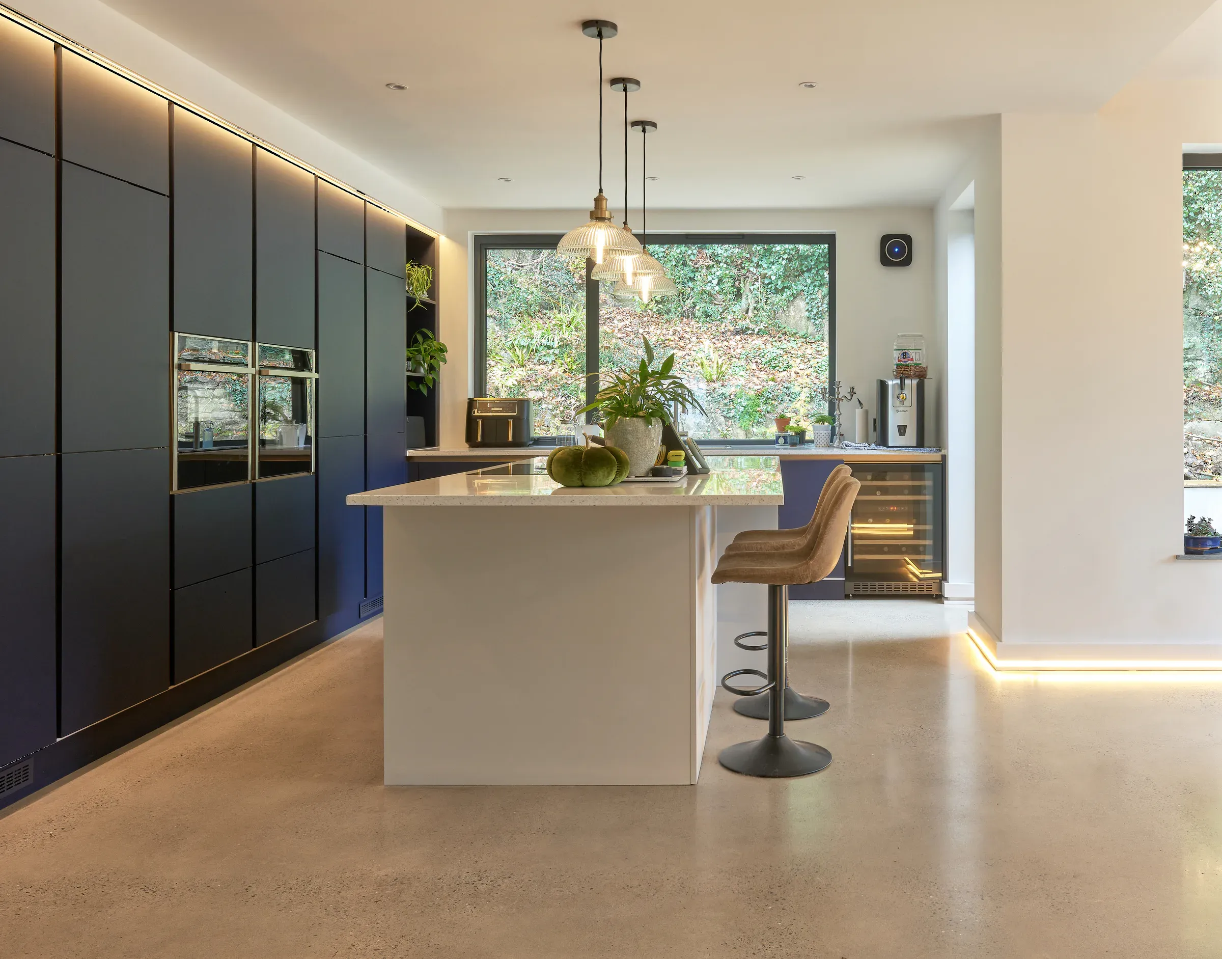 Kitchen island in dark units with under-counter lighting and polished concrete floor