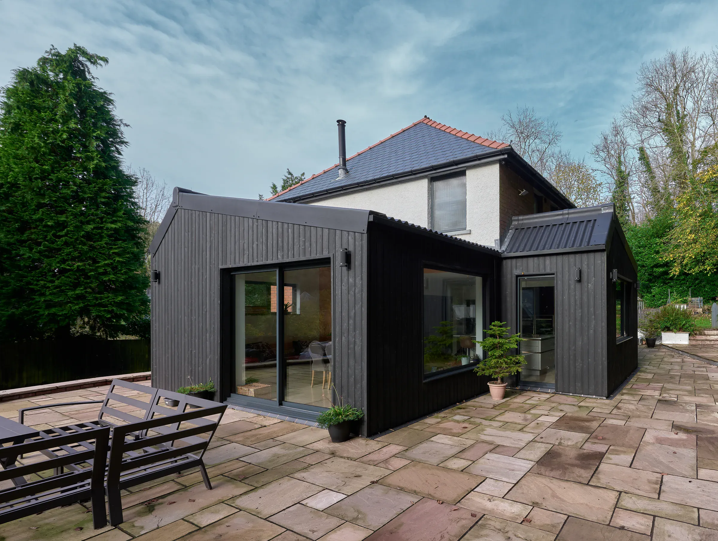 Black timber-clad extensions on a rendered house in Pontypool, with large windows looking onto a paved terrace