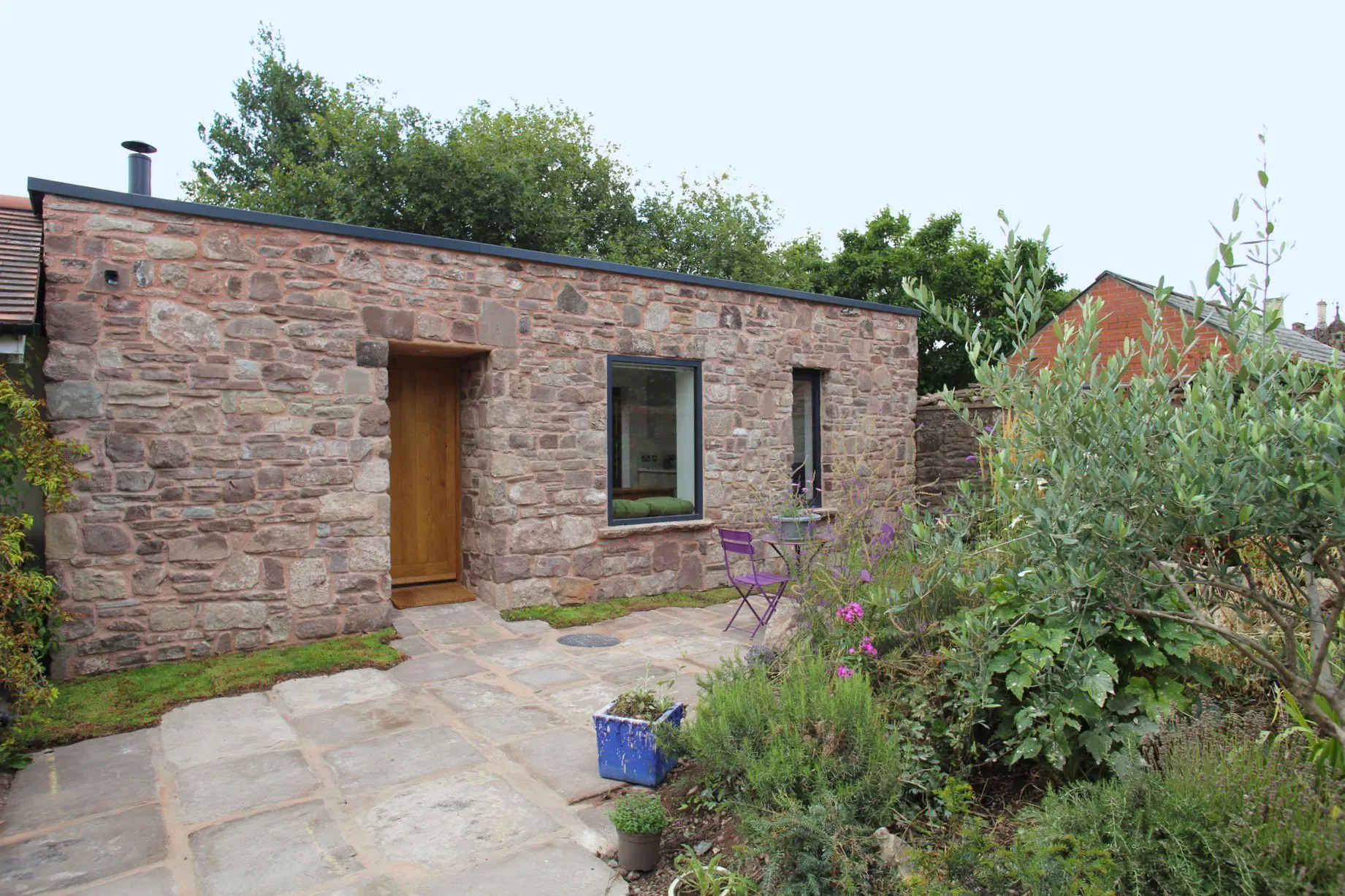Stone-fronted garden room in Monmouth with an oak door and a dark-framed window, set among planting and stone paving