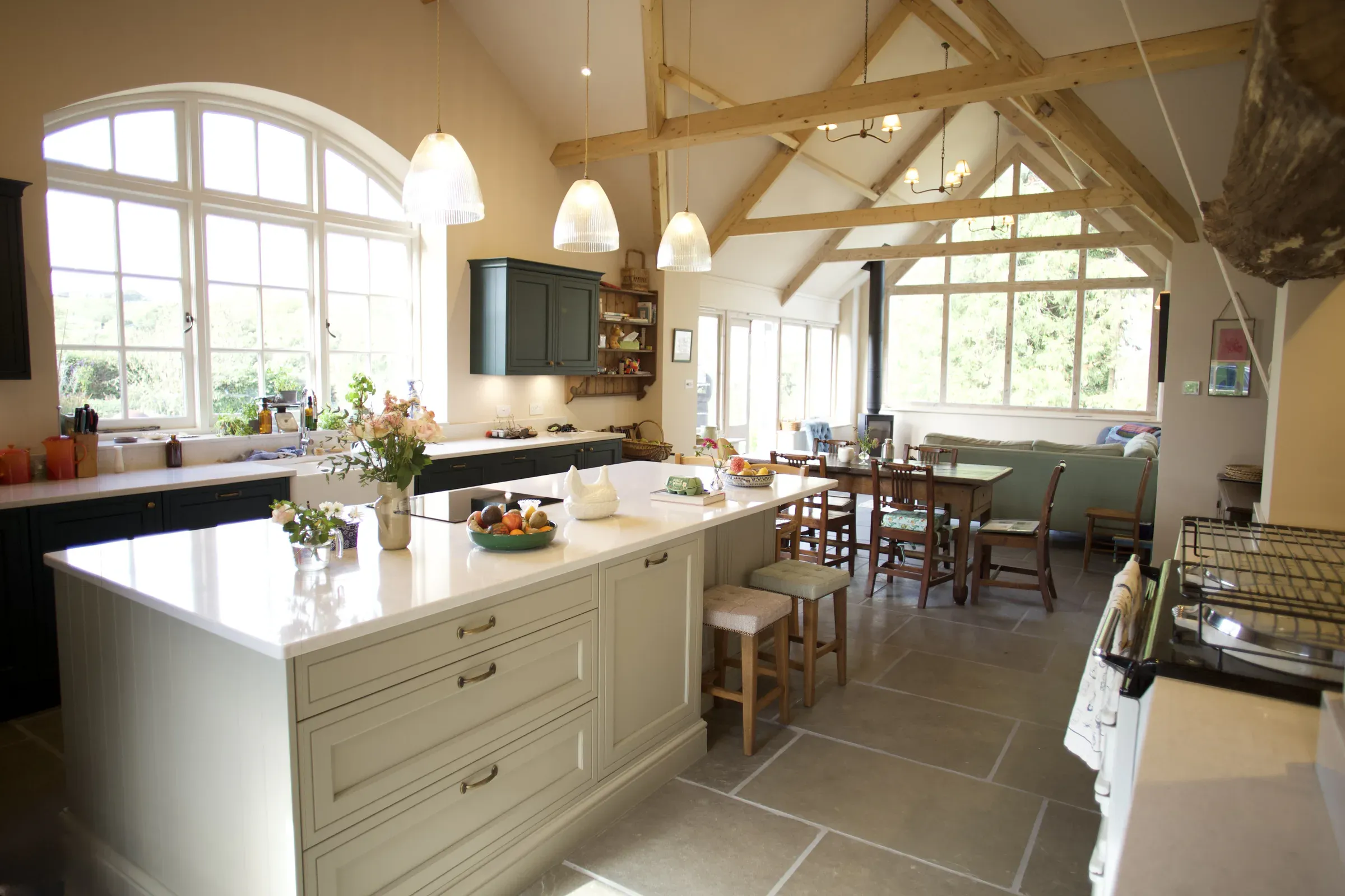 Open-plan kitchen and dining room in a restored farmhouse near Abergavenny, with a vaulted ceiling, exposed oak trusses and a large arched window