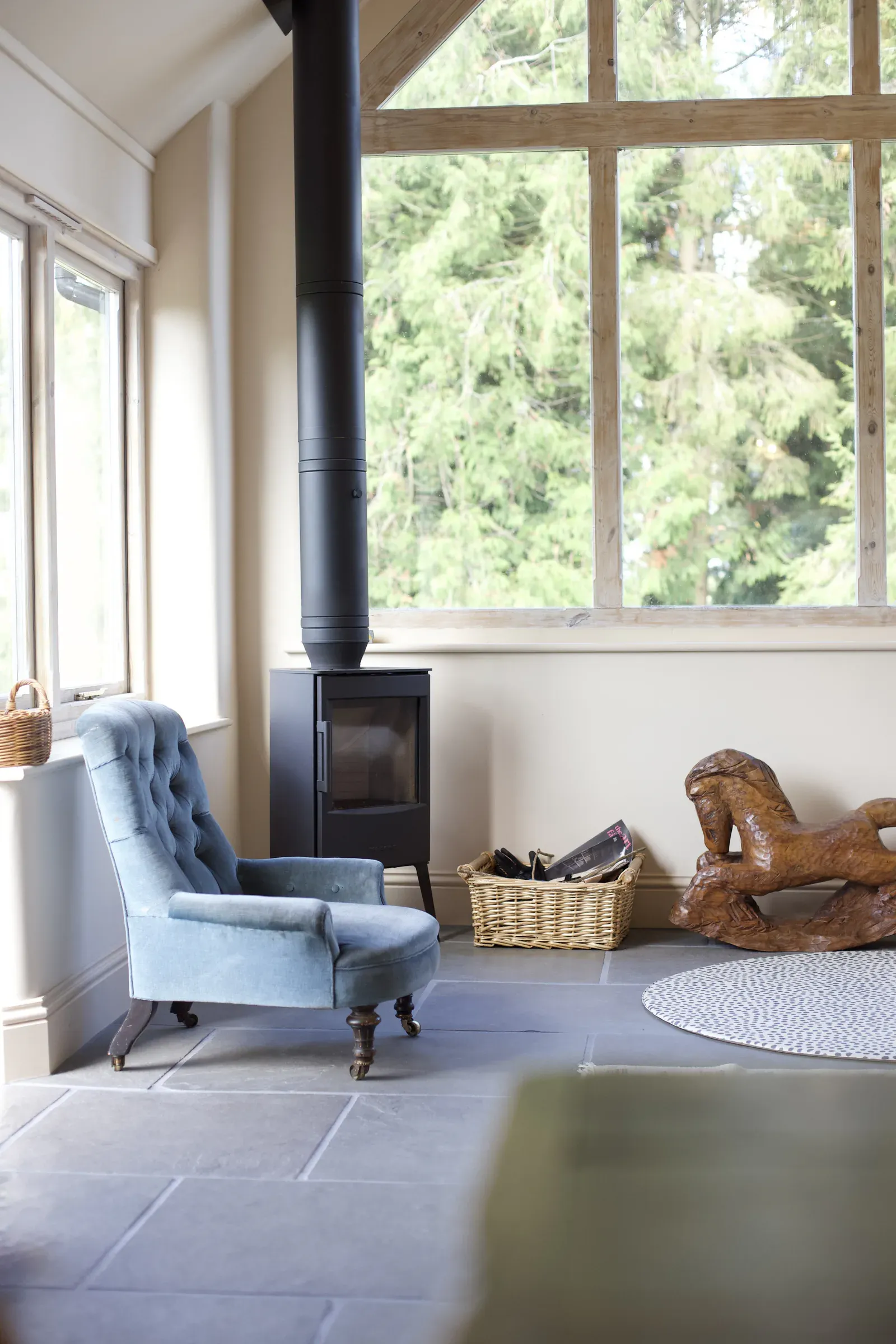 Wood-burning stove in front of a full-height window, with an armchair and flagstone floor