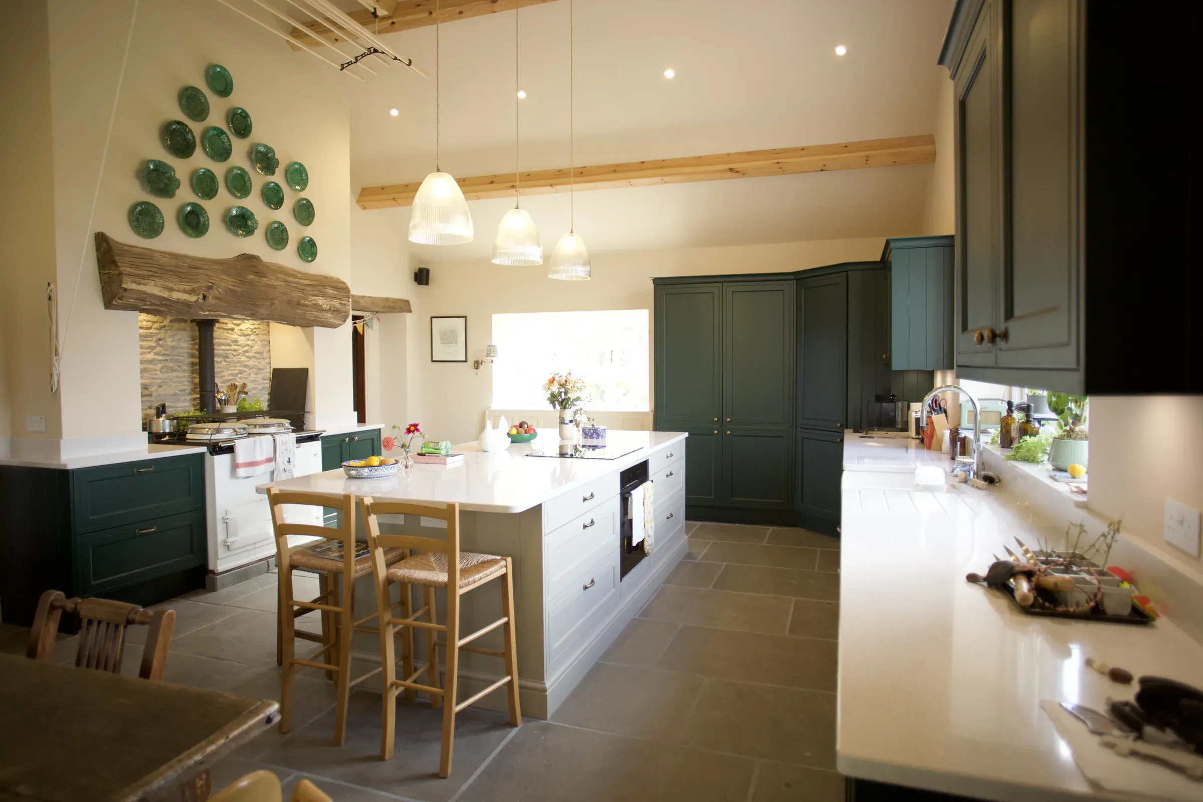 View along the kitchen to the Aga, with green plates on the wall and a fallen-tree beam as the Aga housing