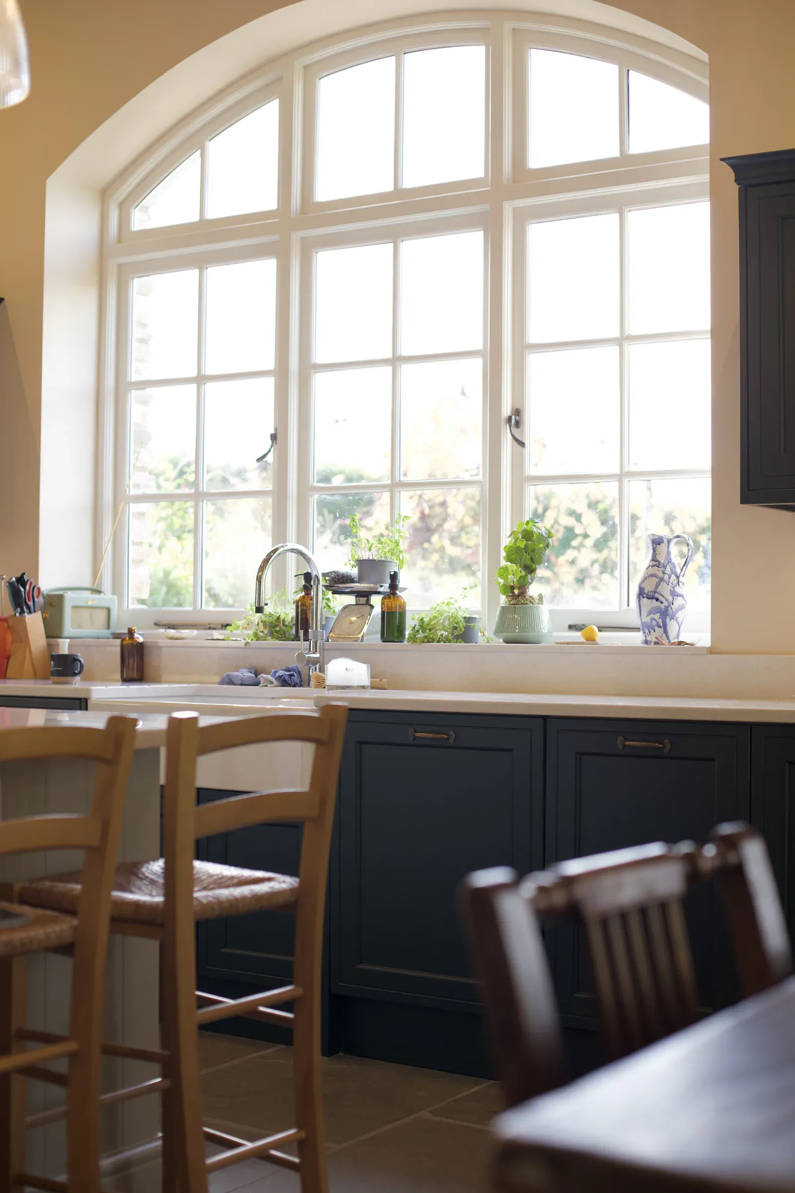 Arched window above the kitchen sink, with dark green units and bar stools at the island
