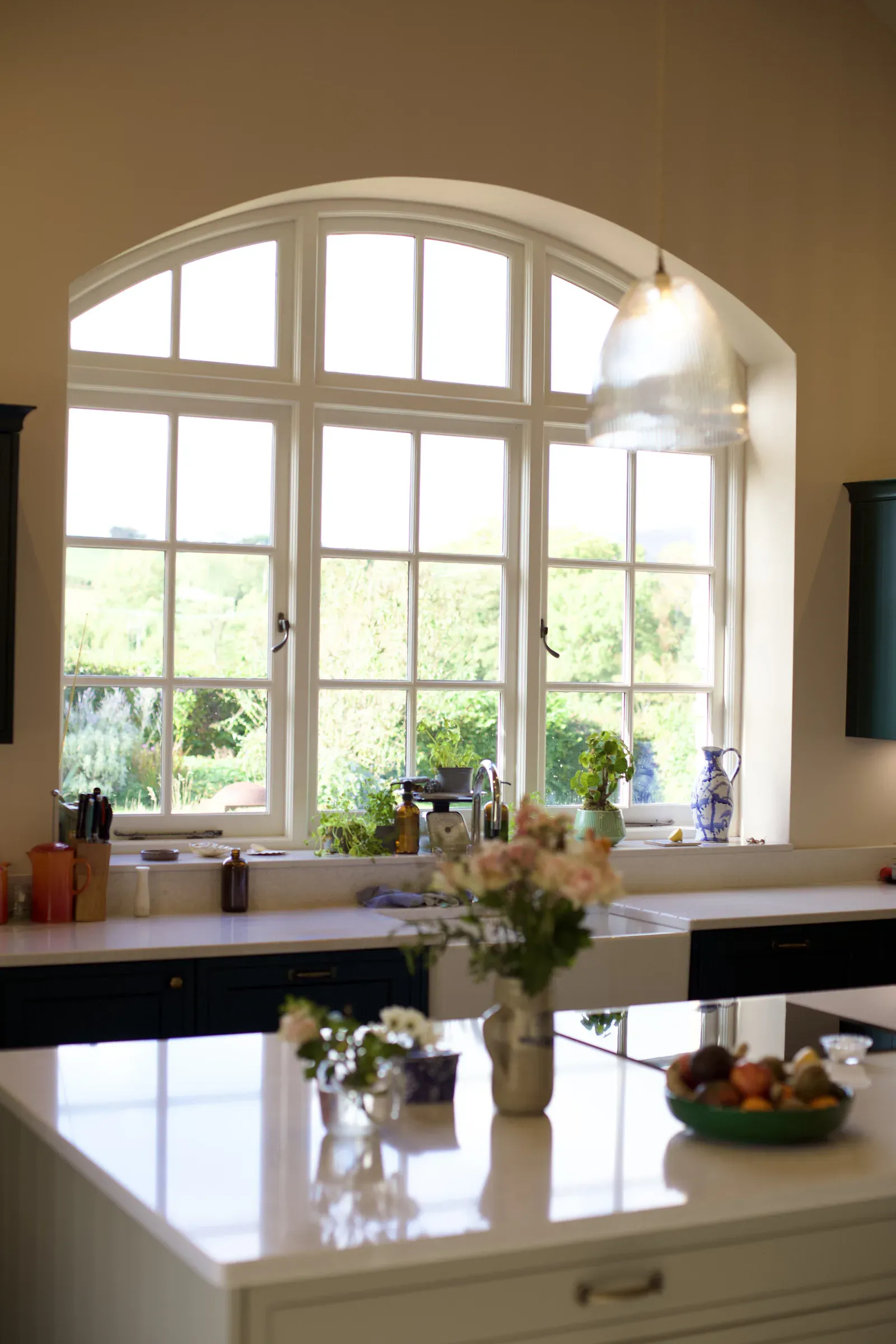 Kitchen island with flowers and fruit, and the arched window beyond