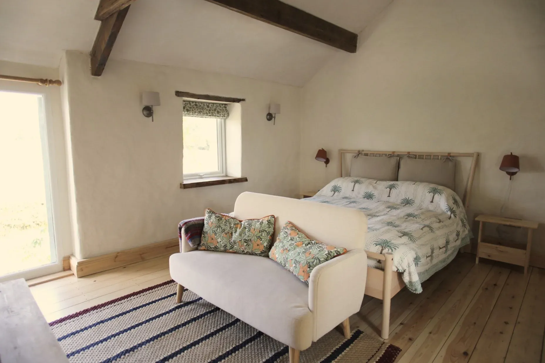 Bedroom in a converted stable near Usk, with lime-plastered walls, an exposed beam and a wide window onto fields