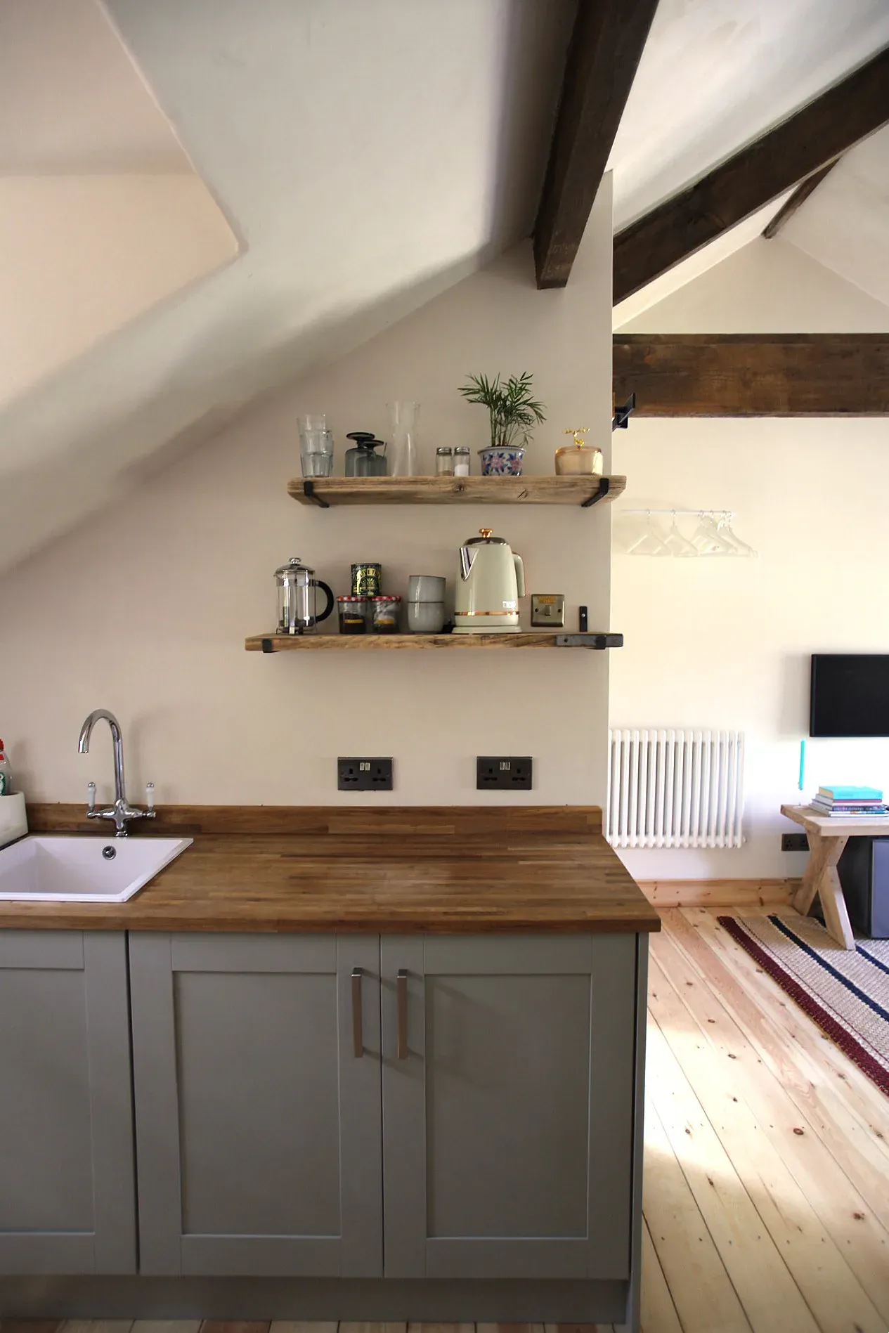 Kitchen with grey units, an oak worktop and open oak shelves beneath an exposed beam