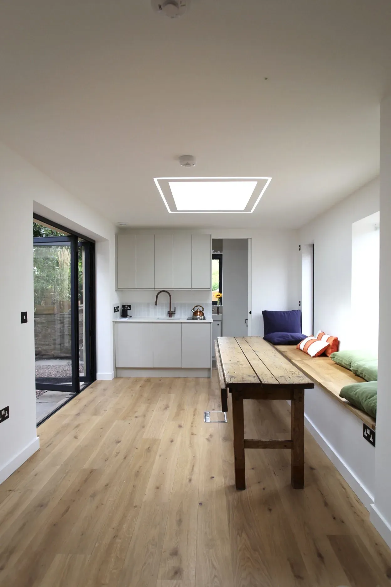 Compact kitchen with white units and an oak table, under the rooflight